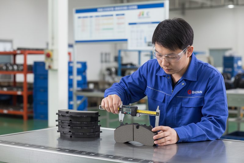 Техник завода BAIYUN Brake проверяет партию тихих керамических тормозных колодок на производственной линии на предприятии, сертифицированном по IATF 16949.